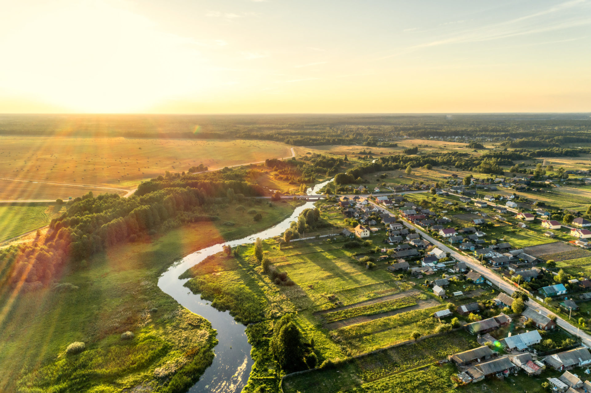 Aerial view. Small european village. Blue winding river. Summer evening, sunny sunset.